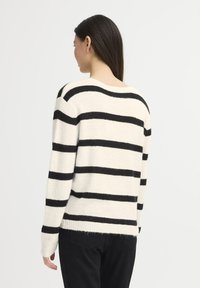 Striped sweater featuring black and cream colors, soft texture, and long sleeves with ribbed cuffs and hemline, viewed from the back.