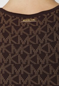 Pull en tricot marron avec un motif texturé de symboles entrelacés 'MK' en doré. Étiquette en laiton avec l'inscription "Michael Kors" au niveau du col.
