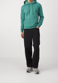 Turkos bomulls-hoodie med framficka och dragsko i huvan, kombinerad med svarta byxor med lös passform. Sneakers med en grå och vit design.