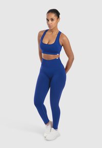 Reggiseno sportivo blu e leggings a vita alta, realizzati in un tessuto morbido ed elastico. Presentano un design aderente con branding minimal e senza motivi.