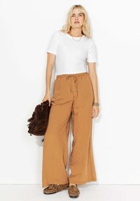 Pantalons larges à rayures brunes avec une taille élastique et un cordon de serrage, associés à un haut ajusté à manches courtes blanc et un sac frangé marron.