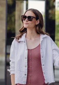 Bílé košilové sako s výšivkou květinových detailů přes růžový žebrovaný top na ramínkách se zdobením knoflíky. Tmavé sluneční brýle v ceně.