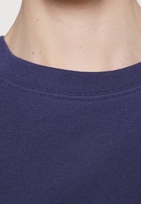 Námořnická modrá bavlněná trička s kulatým výstřihem, hladkým povrchem a čistým švem kolem límce. Zaměřeno na oblast krku.