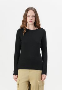 Zwarte fitted top met lange mouwen en ronde halslijn, gemaakt van gladde stof. Draagt bij beige cargo pants, afgebeeld tegen een witte achtergrond.