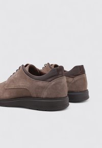 Zapatos de ante marrón con un acabado texturizado, que presentan una puntera redonda, cordones planos y un tacón y lengüeta de color marrón oscuro que contrastan.