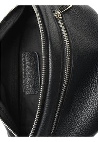 Interno di uno zaino in pelle nera che mostra una superficie strutturata, una tasca con cerniera, fodera in tessuto e una etichetta con il logo "RYLKO".