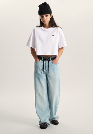 Bílý krátký tričko s malým logem, světle modré volné džíny, černá pletená čepice a černé boty s texturovanou podrážkou.