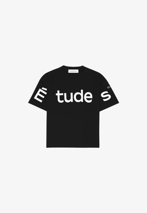 T-shirt noir à manches courtes en coton, arborant un grand texte blanc "Étude" sur le devant et "Studio" sur la manche gauche.