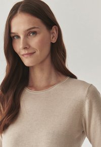 Pull crème à col rond avec une texture lisse, des manches longues et de subtils détails de couture. Le tissu semble doux et léger.