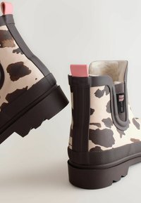 Brune og creme cow-print gummistøvler til anklerne med lyserøde accenter og texturerede såler, der har en blød foring og pull tabs for nem påtagning.