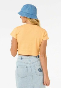 Camiseta naranja de canalé recortada con mangas cortas, combinada con una falda de mezclilla azul claro que presenta un diseño de mariposa bordado en la parte trasera.