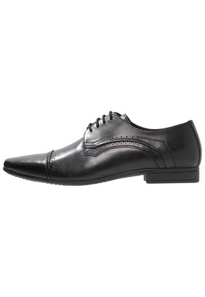 Schwarzer Herrenschuh aus Leder mit spitzer Zehenpartie, Schnürsenkeln, Brogue-Details und niedrigem, gestapeltem Absatz, seitlich dargestellt.