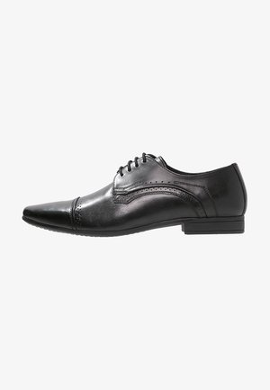 Chaussure habillée pour homme en cuir noir, à bout pointu, avec lacets, détails en brogue et petit talon empilé, vue de côté.