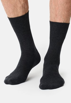 Dunkelgraue Socken bedecken nackte Füße und zeigen eine gerippte Textur. Der Hintergrund ist schneeweiß, was die Schlichtheit der Socken betont.