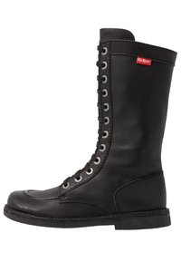 Black leather knee-high boot with a rounded toe, prominent lace-up front, silver eyelets, and a textured rubber sole. Kickers logo visible.