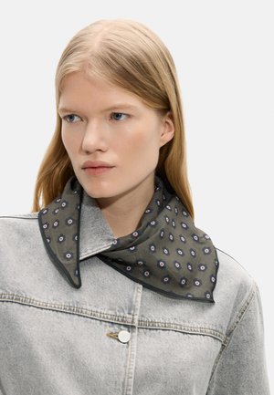 Kobieta o długich blond włosach, ubrana w jasnoszarą kurtkę jeansową i ciemnozielony szalik w wzory zawiązany wokół szyi, patrząca w lewo.