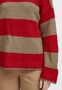 Pullover a righe rosse e beige. Texture morbida e a maglia con maniche larghe e una vestibilità comoda. L'orlo presenta una finitura a coste.