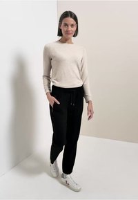 Top beige de manga larga, pantalones jogger negros con cintura elástica y bolsillos laterales, y zapatillas blancas con detalles en rosa. Tejido suave y corte relajado.