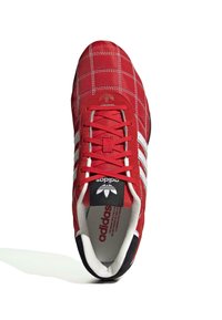 Röd sneaker med quiltat överdrag, som har en vit tre-stripesdesign, vadderad krage och svart sula. Snören i matchande röd.