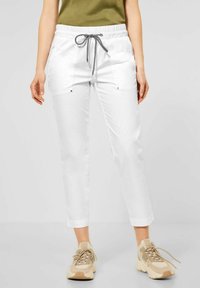 Kvinna som bär vita korta byxor med en svart och vit dragsko, ihop med beige och vita chunky sneakers.