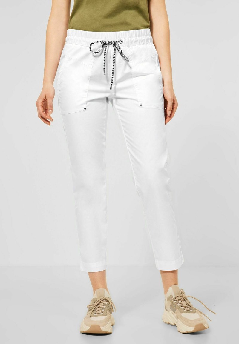 Kvinna som bär vita korta byxor med en svart och vit dragsko, ihop med beige och vita chunky sneakers.