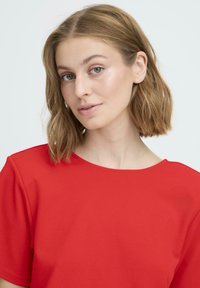 Top rojo de manga corta con escote redondo, textura suave y detalle mínimo de costuras. El modelo muestra una expresión neutral.