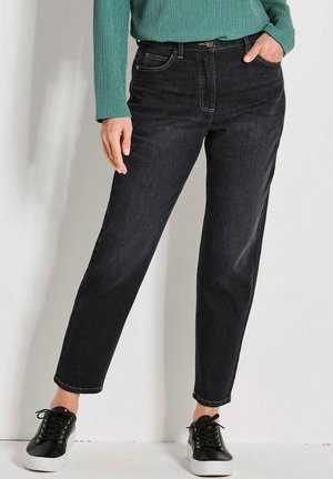 Jeans in denim scuro con taglio dritto, vita alta e quattro tasche, abbinati a sneakers nere e un top verde a trama.