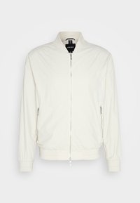 Giacca bomber beige chiaro in tessuto texturizzato, caratterizzata da un colletto alzato, chiusura frontale a zip e tasche laterali con zip. Polsini e orlo a costine.