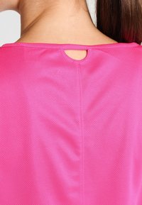 Zbliżenie na górną część pleców osoby noszącej jasnoróżową koszulkę sportową z oddychającego materiału oraz małym wycięciem przy dekolcie.