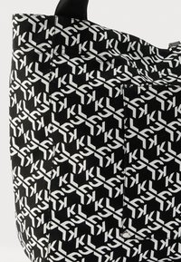 Čierna taška na rúčku s opakujúcim sa bielym logom, obdĺžnikového tvaru, z pevnej látky a so bočným vreckom so strieborným kovaním.