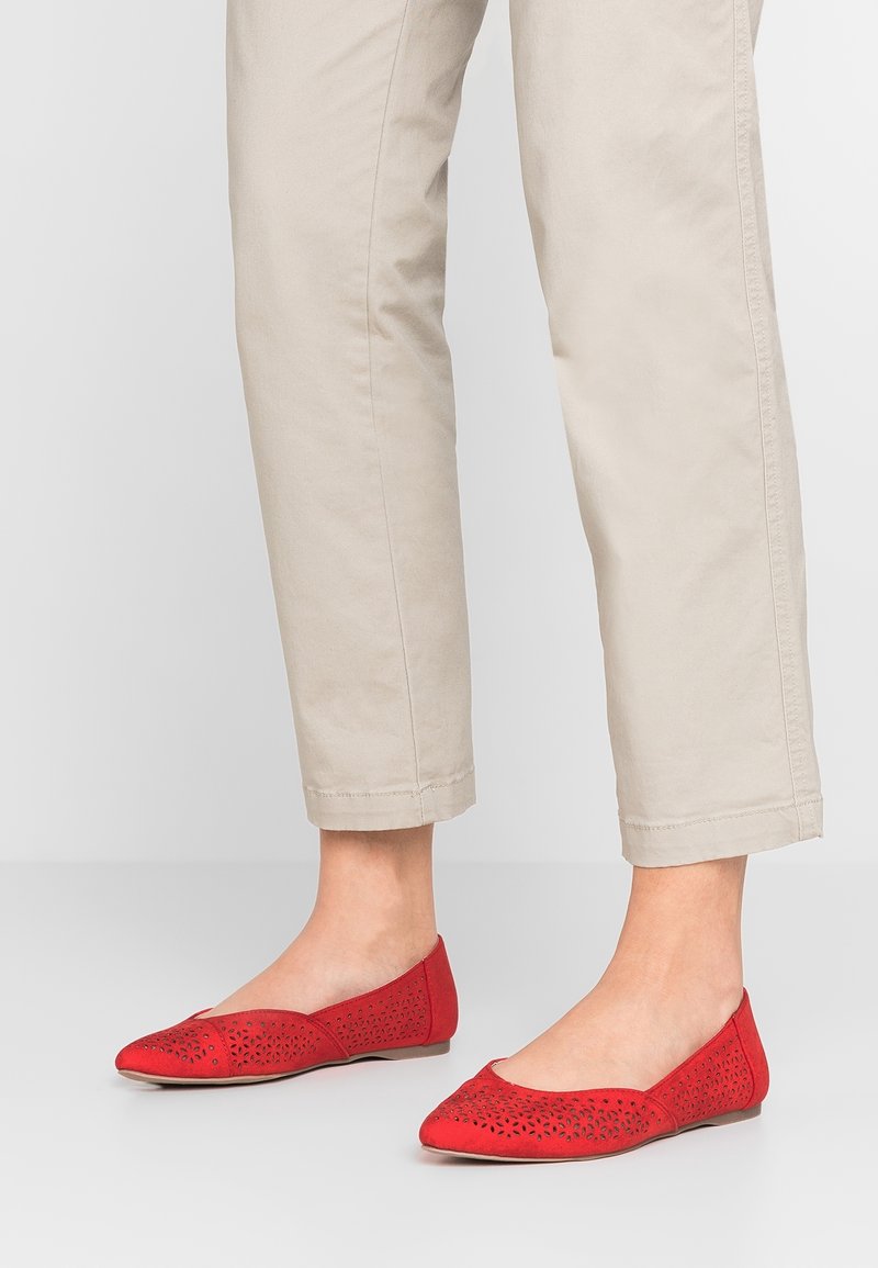 Rote flache Schuhe mit Ausschnittdetails, spitzem Zehenbereich und einem weichen Obermaterial. Kombiniert mit leichten, beige Cropped-Hosen.