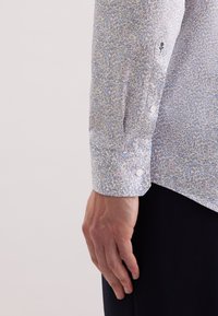 Camicia a maniche lunghe con motivo floreale blu chiaro e polsini con bottoni. Tessuto morbido con piccoli bottoni bianchi e un logo floreale decorativo sulla manica.