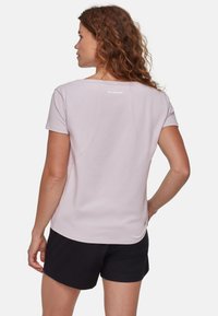 Lichtroze T-shirt met korte mouwen en ronde hals, met een logo op de achterkant en een gladde, lichte stof. Gecombineerd met donkere shorts.