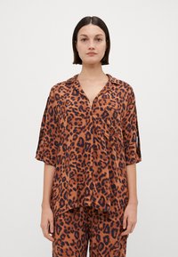 Jakke med leopardmønster i oransje og brune toner, laget av glatt materiale med kragedesign, lomme detalj og løse ermer.