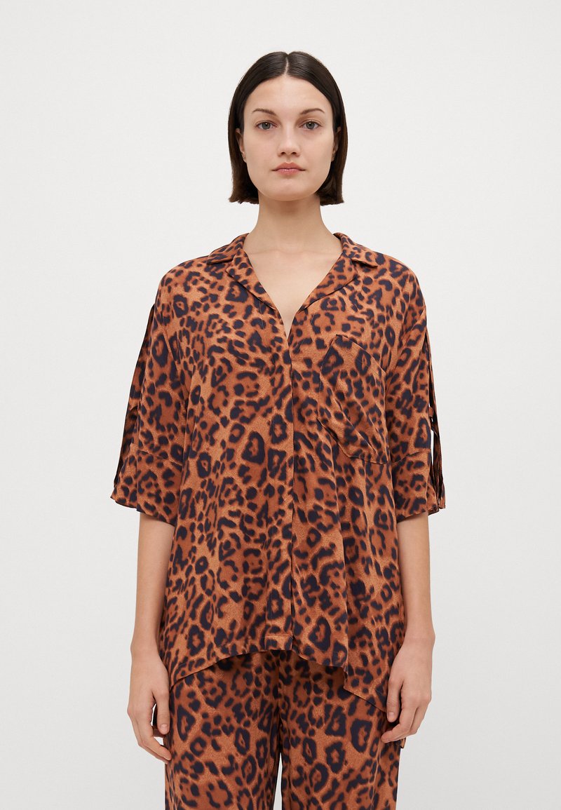 Jakke med leopardmønster i oransje og brune toner, laget av glatt materiale med kragedesign, lomme detalj og løse ermer.