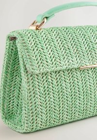Sac à main vert tissé avec un design en tresse texturée, forme rectangulaire, une poignée en cuir et une fermeture à fermoir accentuée en or.