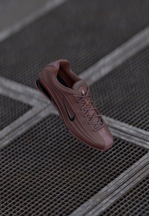 Svetloružová športová topánka s textúrovaným sieťovaným zvrškom, čiernymi akcentmi a šnurovacím dizajnom. Obsahuje odpruženie odolné voči nárazom a aerodynamický tvar.