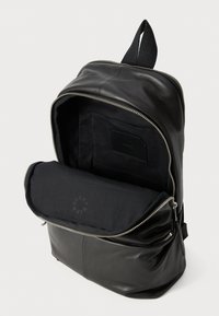Black leather backpack with a smooth texture, zippered opening, and a spacious interior featuring a black fabric lining and interior pocket.