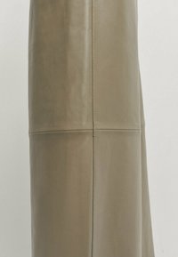 Gros plan d'un vêtement en cuir beige montrant des coutures cousues verticales et horizontales sur un matériau lisse et texturé.