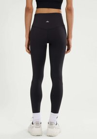 Hoge zwarte leggings van rekbaar materiaal. Uitgerust met een klein logo op de achterkant, een naadloos ontwerp en een figuurvormende silhouet.
