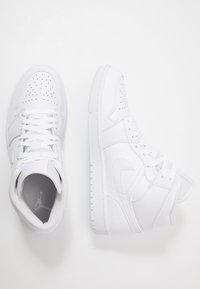 Vita högskor gjorda av texturerat läder med perforerad tå, platta snörningar och en distinkt logo på tungan och sidan.