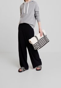 Sweat-shirt gris avec cordons blancs, pantalon noir à jambes larges, et sac à main rayé noir et blanc. Les sandales présentent des rayures assorties.