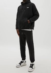 Sweat à capuche noir avec poche avant et cordon de serrage, accompagné d'un pantalon de jogging noir assorti. Les deux sont en tissu doux, avec une coupe décontractée.