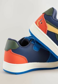 Kolorowe sneakersy z niebieskimi, zielonymi i czerwonymi sekcjami, z grafiką uśmiechniętej buźki z boku, przedstawione z góry.