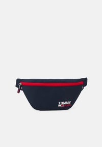 Marinblå midjeväska med röd dragkedja, tillverkad av hållbart tyg. Har en Tommy Jeans-logotyp i vitt, med en snygg, böljande design.
