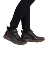 Chaussures en cuir marron à enfiler avec une fermeture éclair sur le côté, finition texturée et semelle en caoutchouc dotée d'un motif. Des lacets ajoutent un détail décoratif.