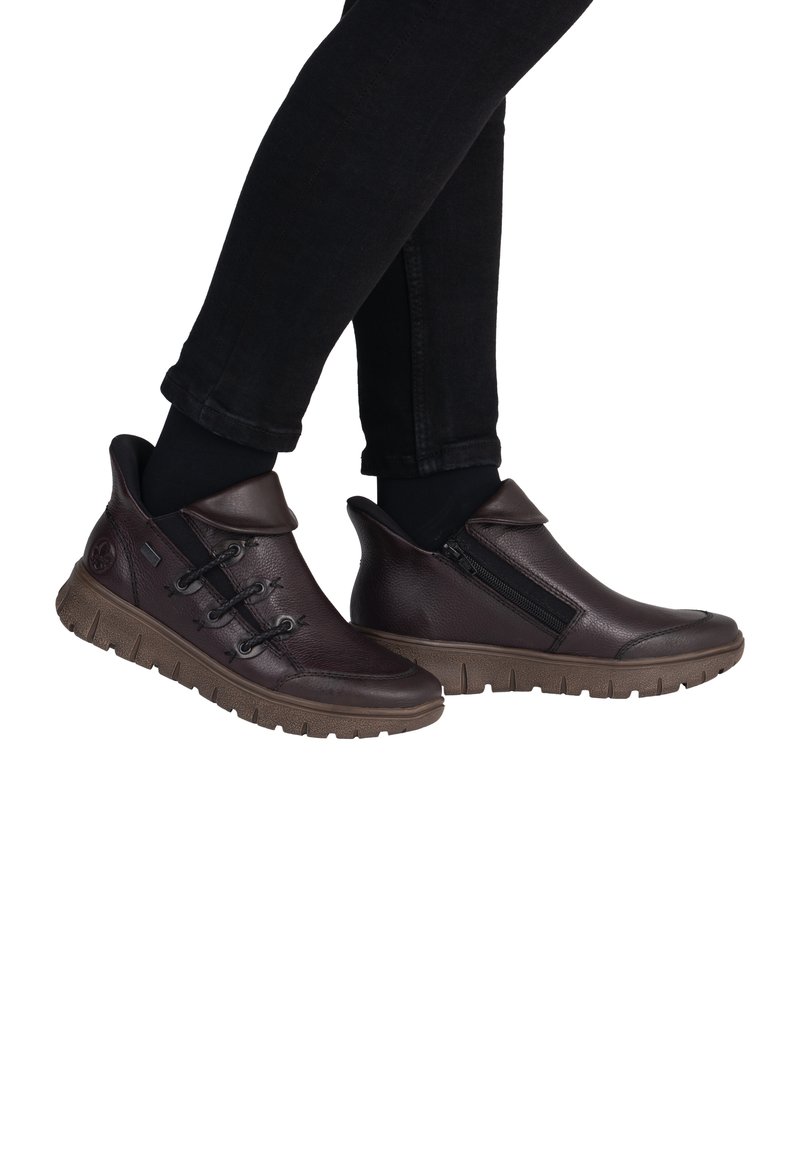 Chaussures en cuir marron à enfiler avec une fermeture éclair sur le côté, finition texturée et semelle en caoutchouc dotée d'un motif. Des lacets ajoutent un détail décoratif.