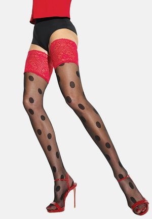 Jambes portant des bas noirs transparents montants jusqu'aux cuisses avec de gros pois noirs et des bordures en dentelle rouge, associés à des sandales rouges à talons hauts.