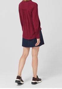 Bordeaux långärmad blus med veck bak, tillsammans med en marinblå denimkjol och svarta mönstrade sneakers med vita sulor.