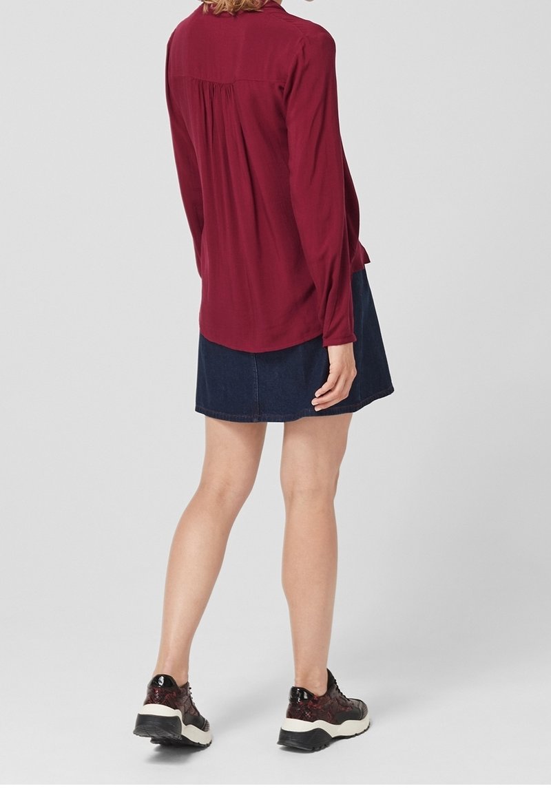 Bordeaux långärmad blus med veck bak, tillsammans med en marinblå denimkjol och svarta mönstrade sneakers med vita sulor.